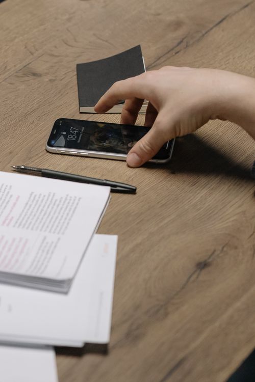 スマートフォンと書類を確認する手元。イメージ写真
